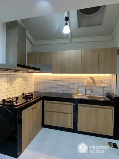 Modern kitchen with sleek black and wood cabinetry, gas stove, and stylish backsplash