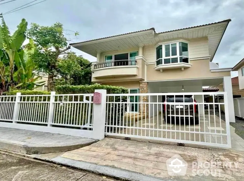 Charming two-story house with gated driveway and lush greenery in a serene neighborhood.