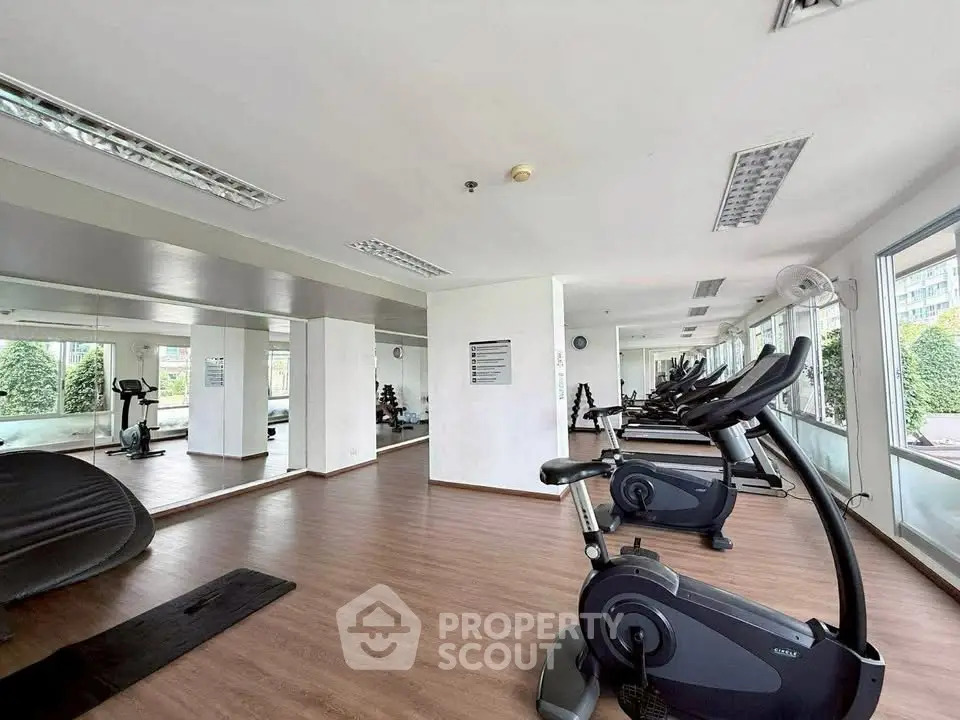 Spacious gym with modern exercise equipment and large windows offering natural light.