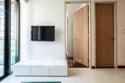 Modern living room with wall-mounted TV and sleek furniture, featuring large windows for natural light.