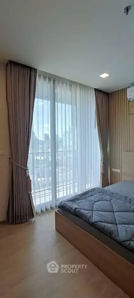Bright bedroom with large window and city view, featuring modern decor and cozy ambiance.