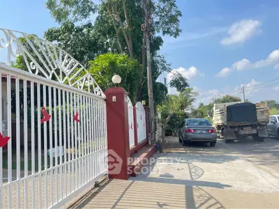 Charming gated entrance with driveway and lush greenery under a clear blue sky.