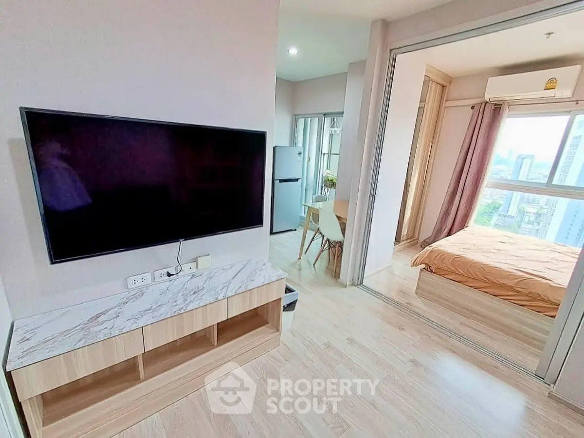 Modern apartment interior with open living room and bedroom, featuring sleek TV setup and city view.