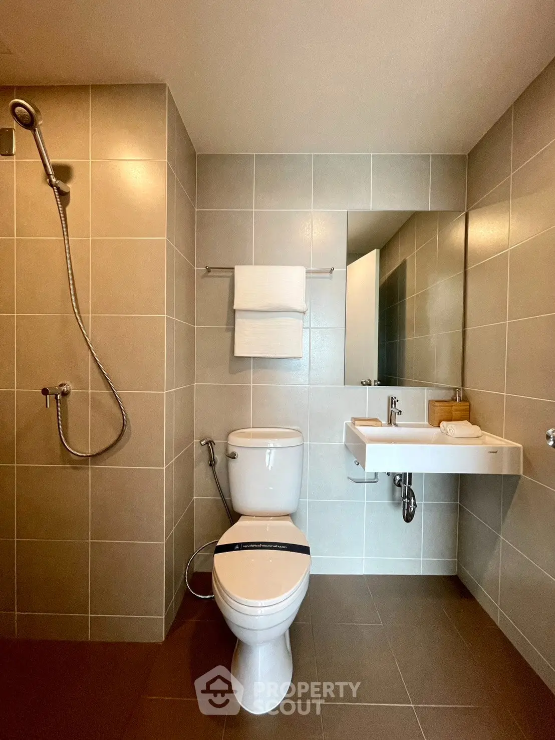 Modern bathroom with sleek fixtures and neutral tiles, featuring a shower and wall-mounted sink.