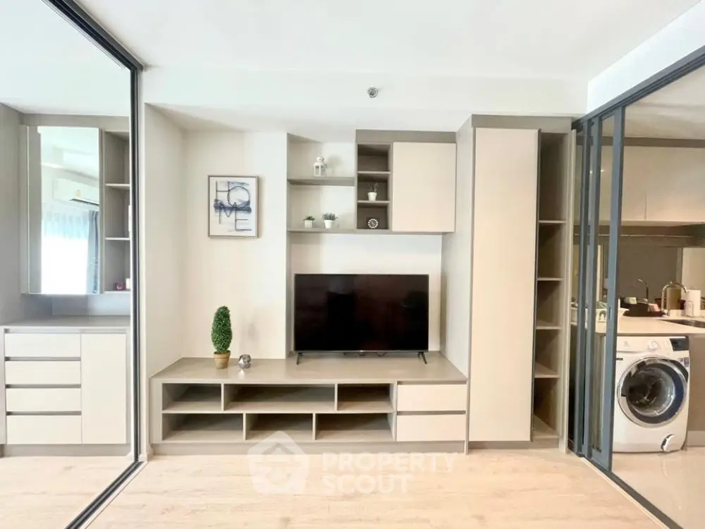 Modern apartment interior with integrated living space, featuring sleek built-in entertainment unit, adjacent to a well-equipped kitchen with washing machine.