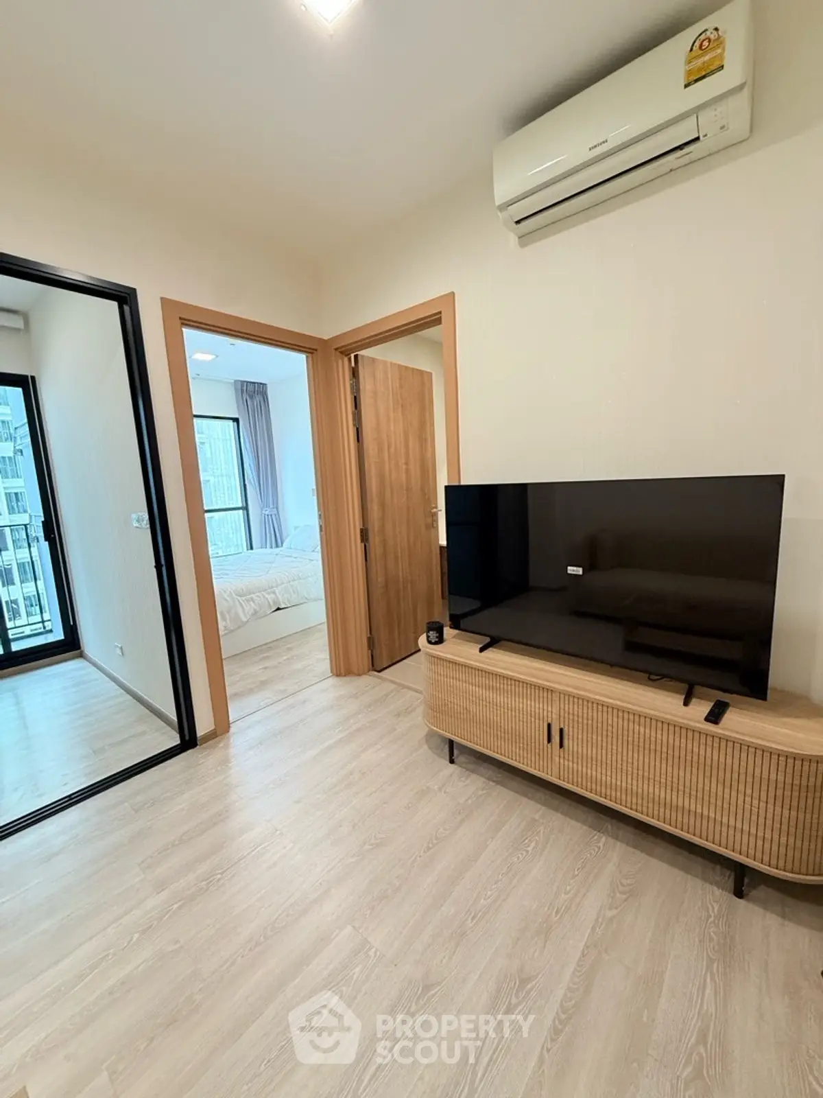 Modern living room with sleek TV stand and air conditioning, leading to a cozy bedroom with natural light.