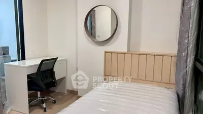 Cozy bedroom with modern desk and chair, featuring a stylish round mirror and natural light.