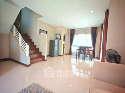 Spacious living area with modern staircase and dining space, featuring large windows and elegant decor.