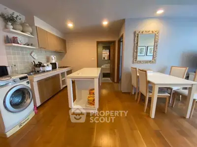 Modern kitchen with wooden flooring, dining area, and washing machine in a cozy apartment.
