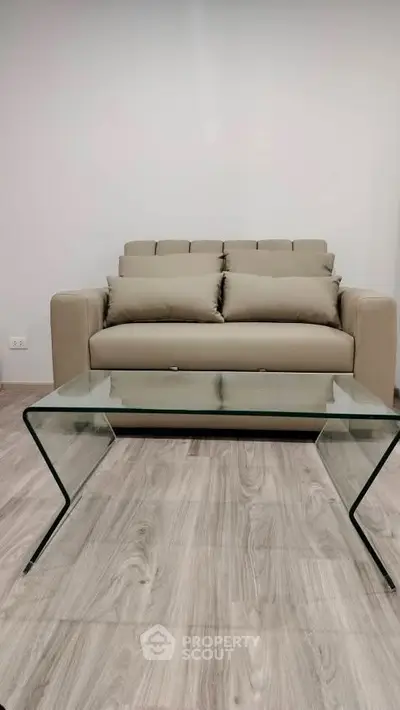 Modern living room with stylish beige sofa and glass coffee table on wooden floor.