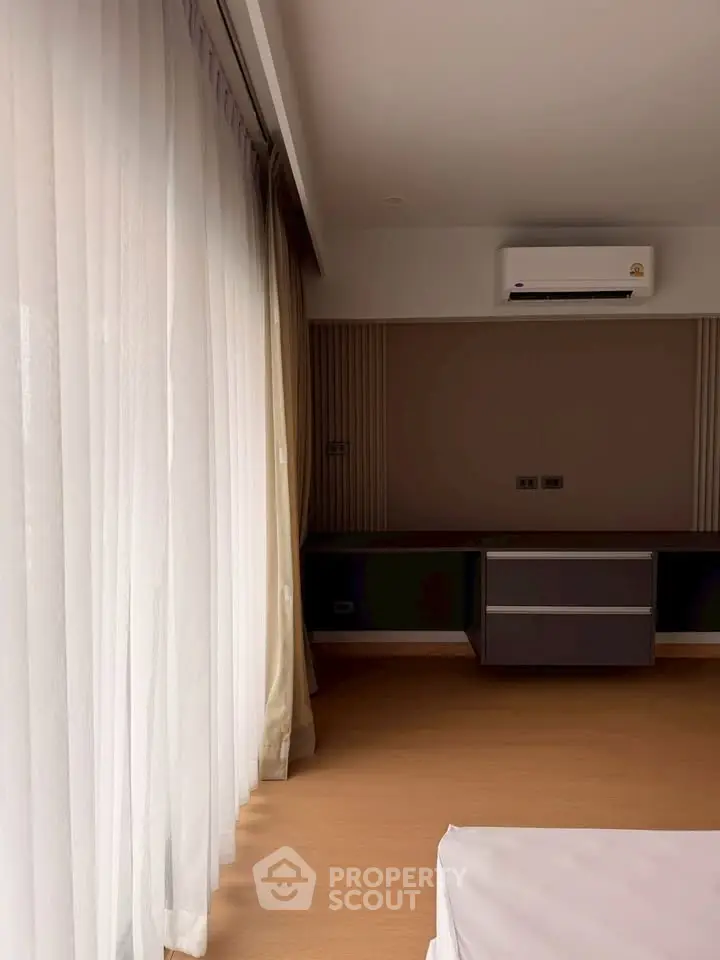Spacious bedroom with large windows and modern air conditioning unit, offering ample natural light and comfort.