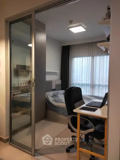 Modern bedroom with sliding glass door and workspace, featuring cozy bed and natural light.