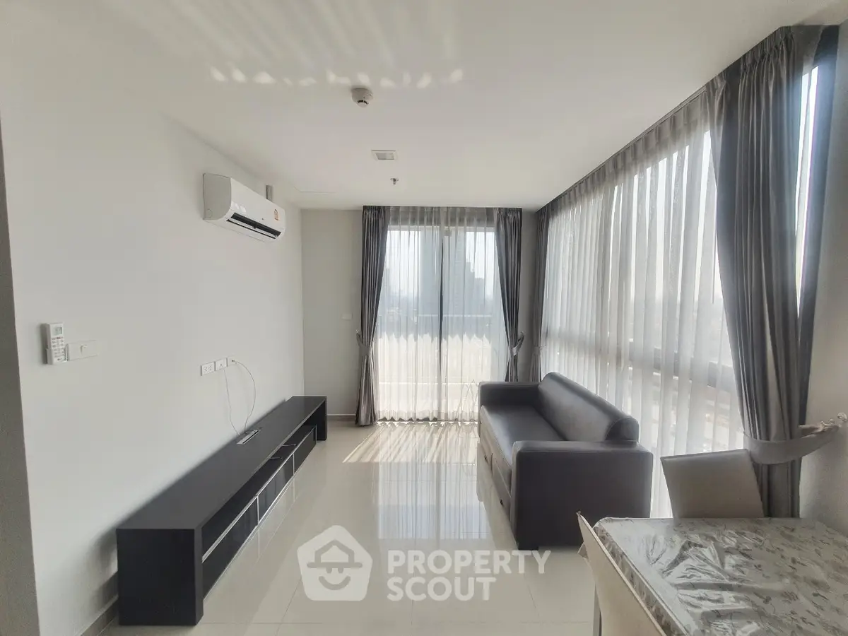 Modern living room with large windows and sleek furniture in a high-rise apartment.