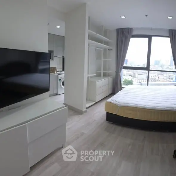 Modern bedroom with large window and city view, featuring sleek furniture and neutral tones.