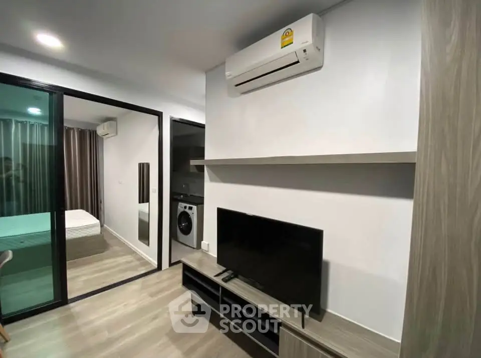 Modern apartment interior with air conditioning, TV, and washing machine, featuring a sleek bedroom view.