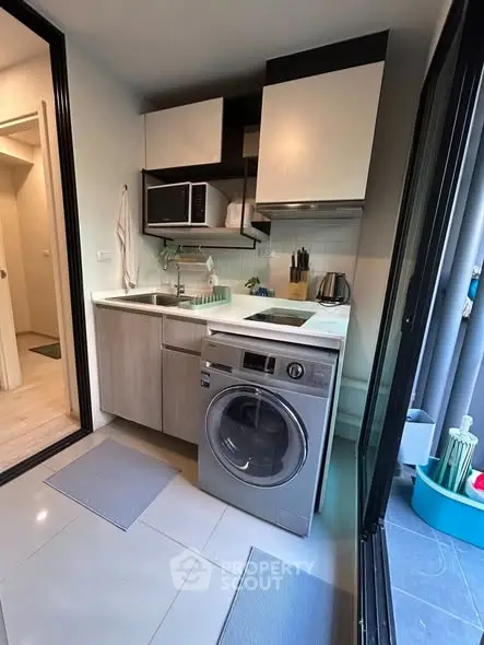 Compact modern kitchen with washing machine and microwave, ideal for urban living.
