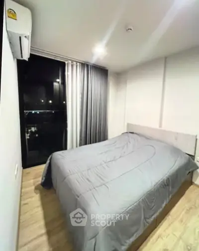 Cozy bedroom with modern decor and large window offering night city view.