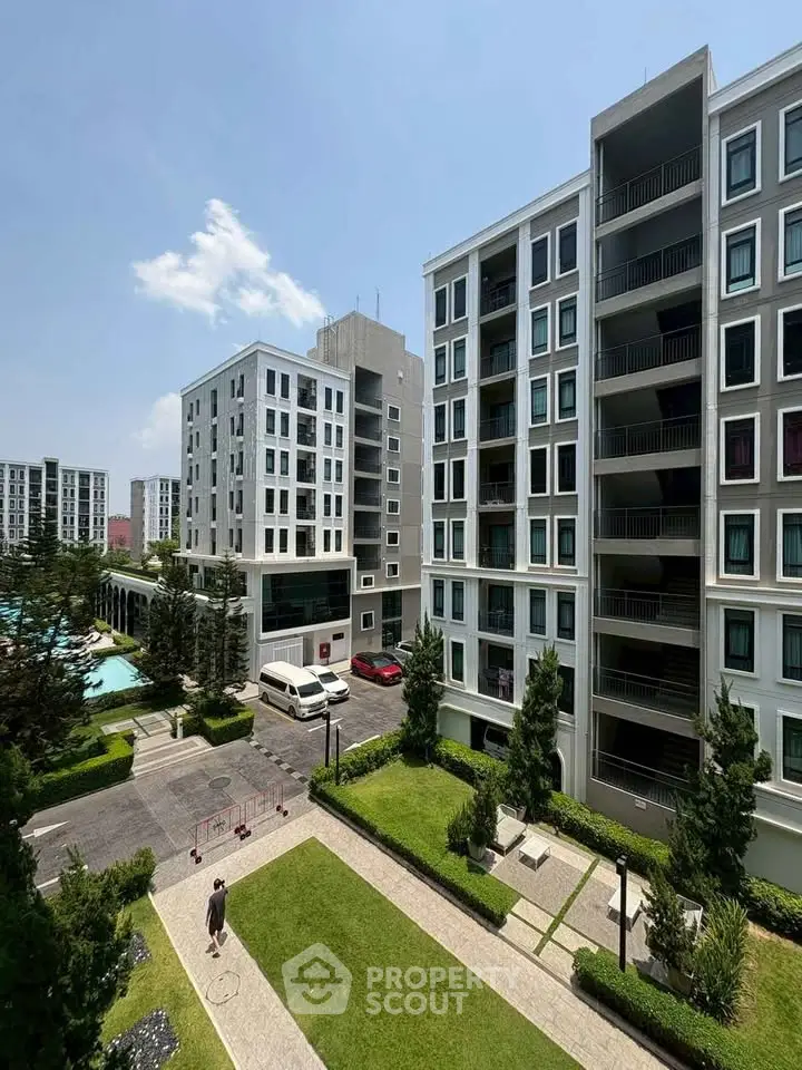 Modern apartment complex with lush gardens and pool view under clear blue sky.
