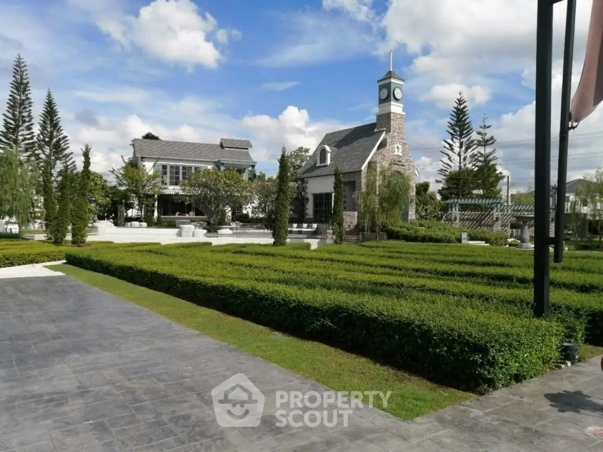 Charming estate with manicured gardens and clock tower under blue skies.
