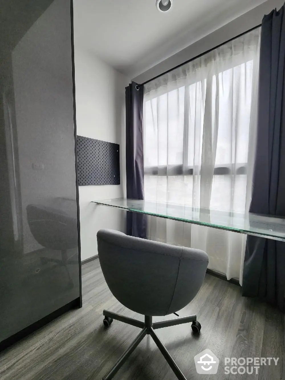 Modern study room with glass desk and ergonomic chair, featuring floor-to-ceiling window for natural light.