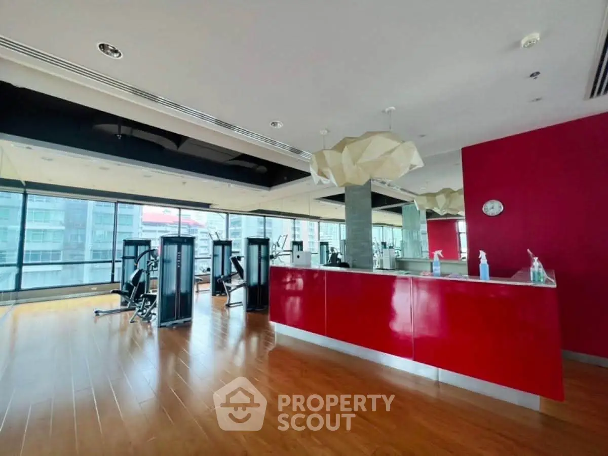 Spacious modern gym with red accents and city view, perfect for fitness enthusiasts.