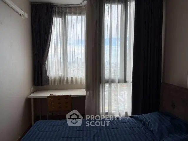 Cozy bedroom with city view, featuring a bed and study desk by large windows.