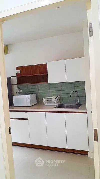 Modern compact kitchen with sleek cabinetry and green tile backsplash, featuring a microwave and sink.