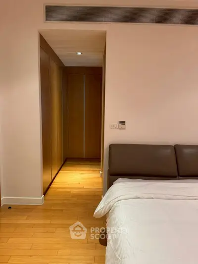 Modern bedroom with wooden flooring and sleek design, featuring a cozy bed and built-in wardrobe.