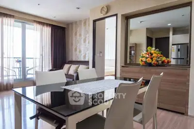 Modern dining area with elegant table, chairs, and floral centerpiece, adjacent to a cozy living room and balcony view.