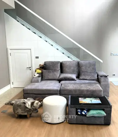 Modern living room with stylish gray sofa and unique decor under a sleek staircase.