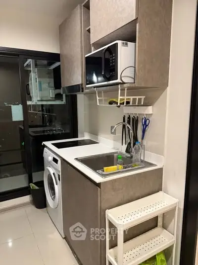 Modern compact kitchen with washing machine and microwave in sleek apartment.