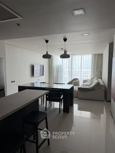 Modern open-layout living room with sleek kitchen and large windows offering natural light.