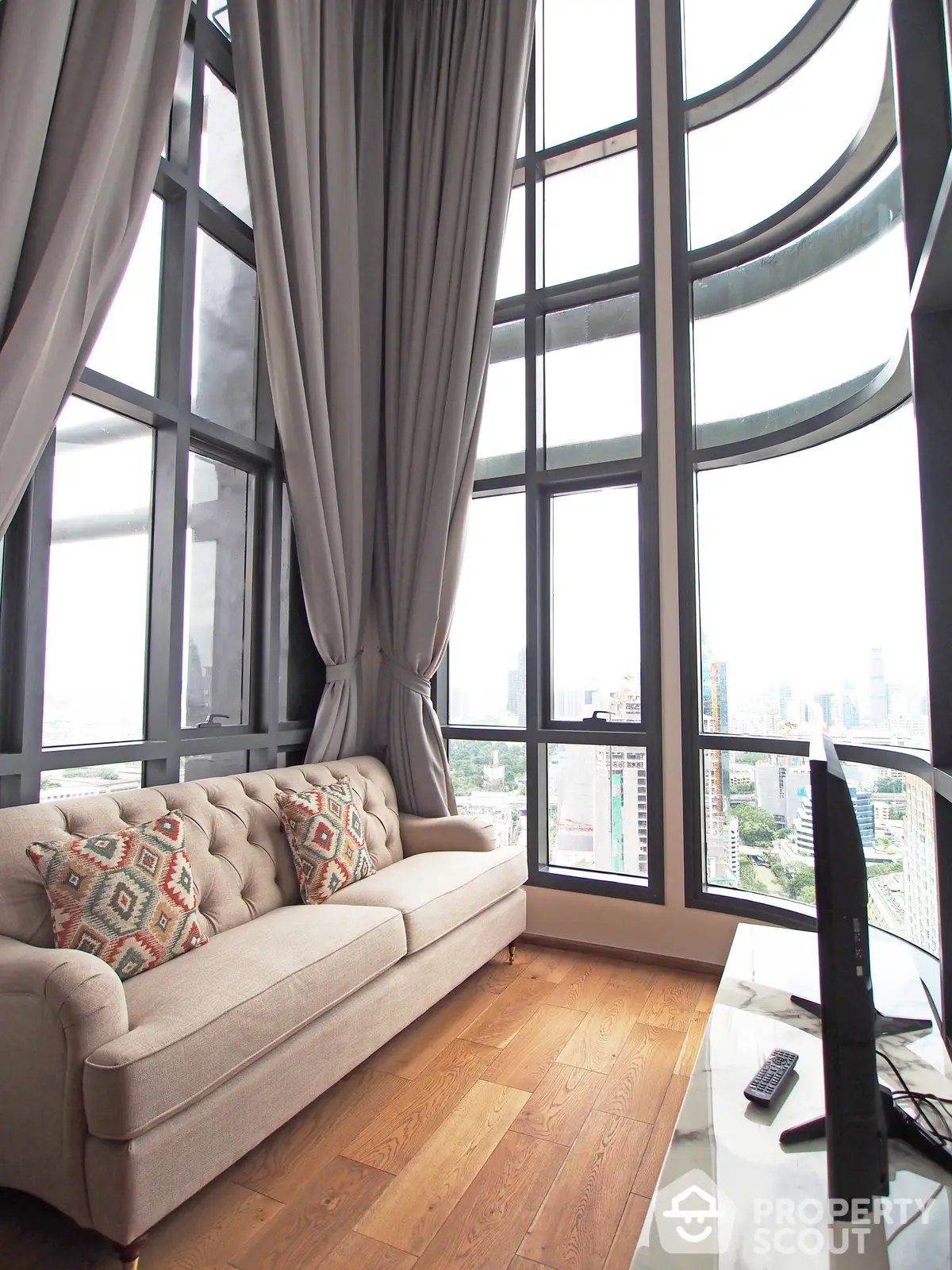 Luxurious high-rise living room with floor-to-ceiling windows offering panoramic city views, elegant drapery, and a plush sofa.