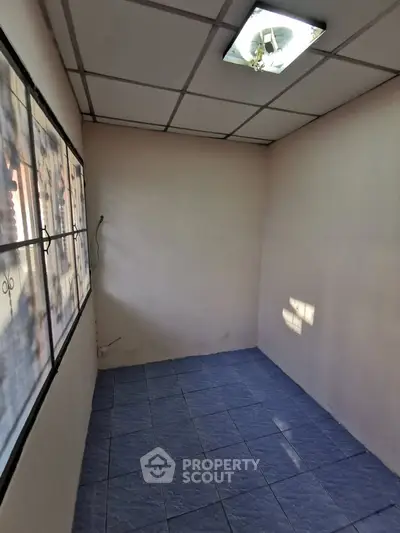 Compact room with tiled floor and large window, ideal for storage or small office space.