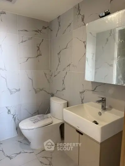 Modern bathroom with marble tiles, sleek sink, and toilet in a contemporary real estate property.