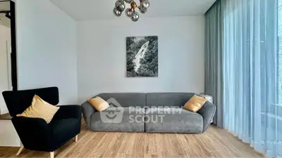 Modern living room with stylish furniture and large window, featuring a cozy gray sofa and elegant armchair.