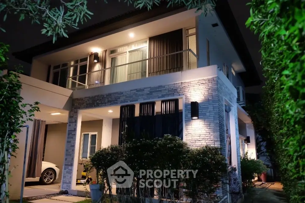 Stunning modern two-story house with elegant lighting and lush greenery at night.