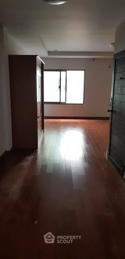Spacious empty room with wooden flooring and large window, perfect for customization.