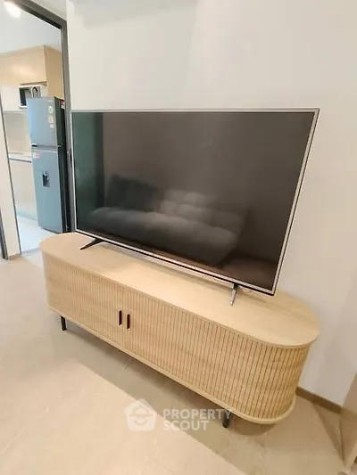 Modern living room with sleek TV stand and flat-screen TV, adjacent to a stylish kitchen area.