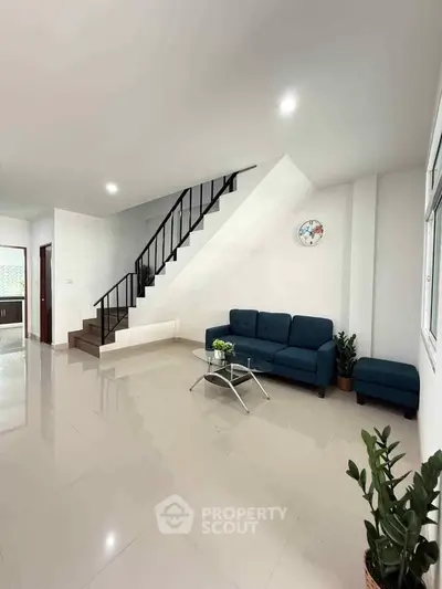 Modern living room with sleek staircase and stylish blue sofa in a bright, open space.