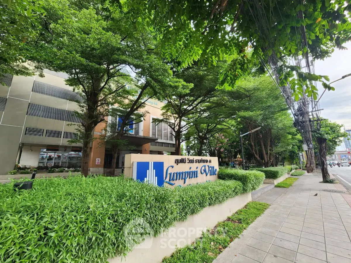Lush greenery surrounds Lumpini Ville building entrance, showcasing modern urban living.