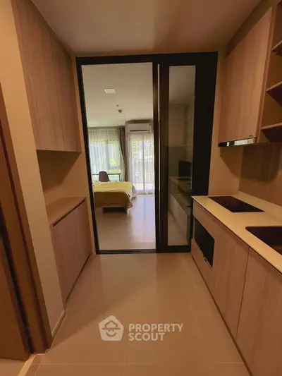 Modern kitchen with wooden cabinets leading to a cozy bedroom with natural light.