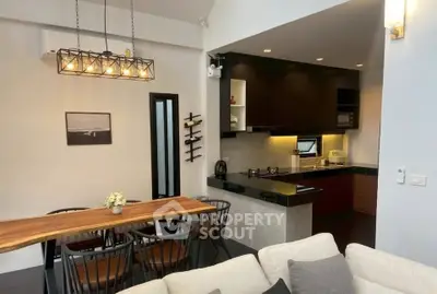 Modern open-plan living room and kitchen with stylish lighting and wooden dining table.