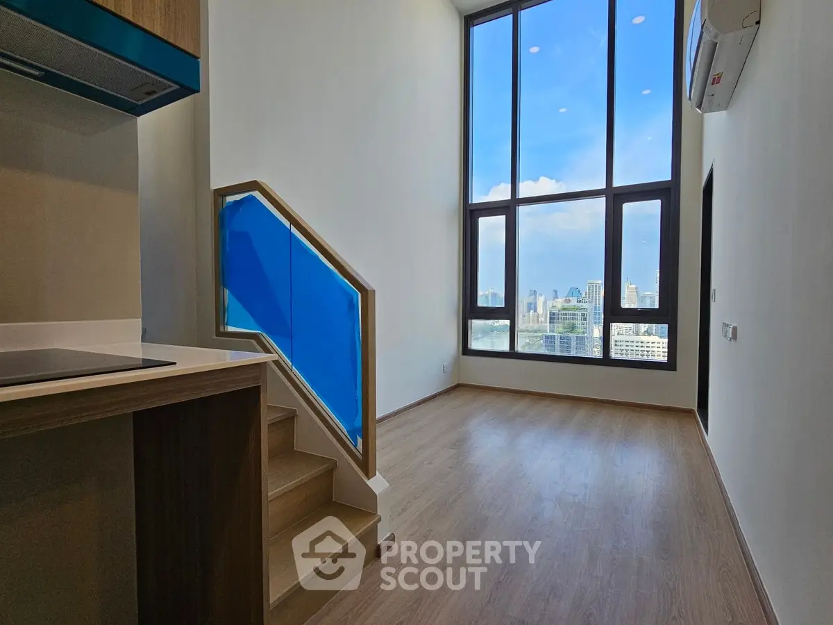 Spacious modern living room with high ceilings and city view, featuring wooden flooring and stylish staircase.