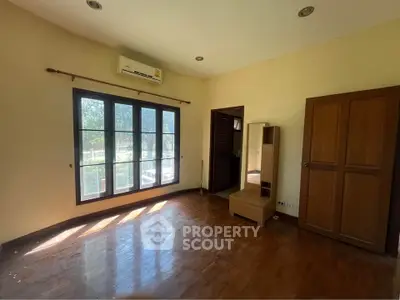 Spacious empty room with wooden floors and large window, perfect for customization.