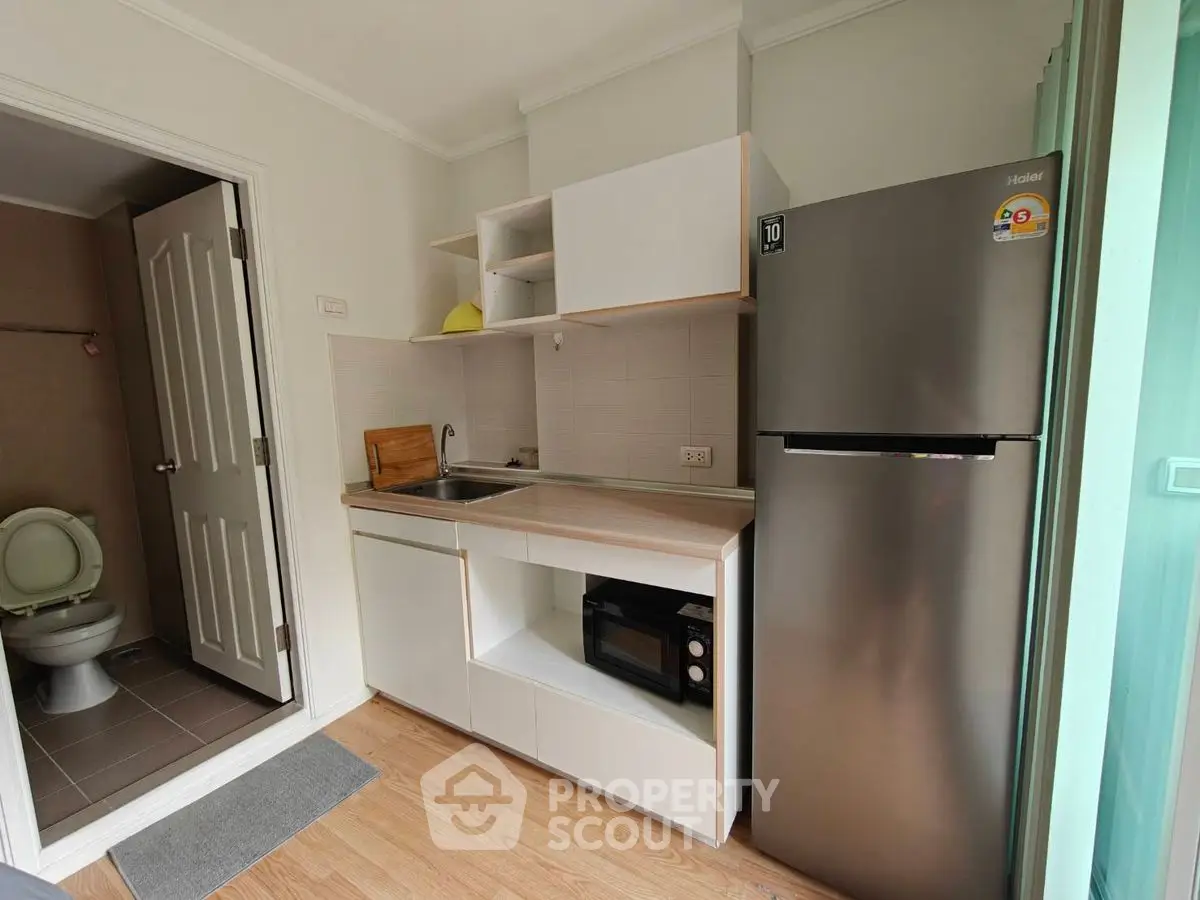 Compact kitchen with modern appliances and adjacent bathroom in cozy apartment.