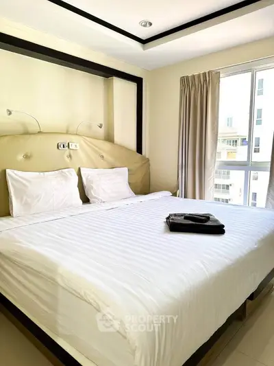 Spacious bedroom with large window and modern decor in a high-rise apartment.