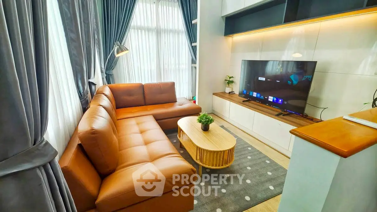 Modern living room with leather sofa and large TV, featuring elegant curtains and cozy decor.