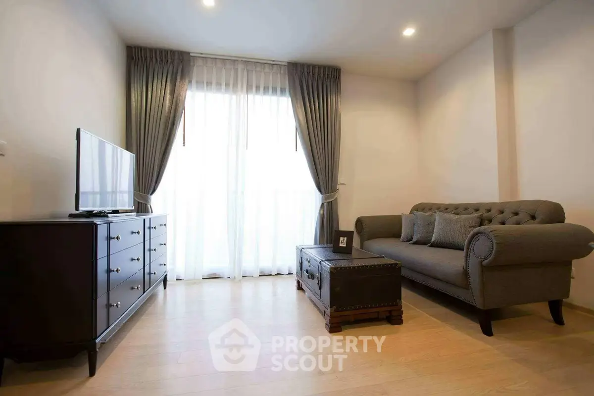 Elegant living room with stylish sofa and TV, featuring natural light through large window.