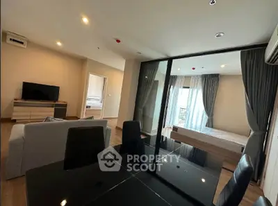 Modern open-plan living room with dining area and bedroom, featuring sleek furniture and large windows.